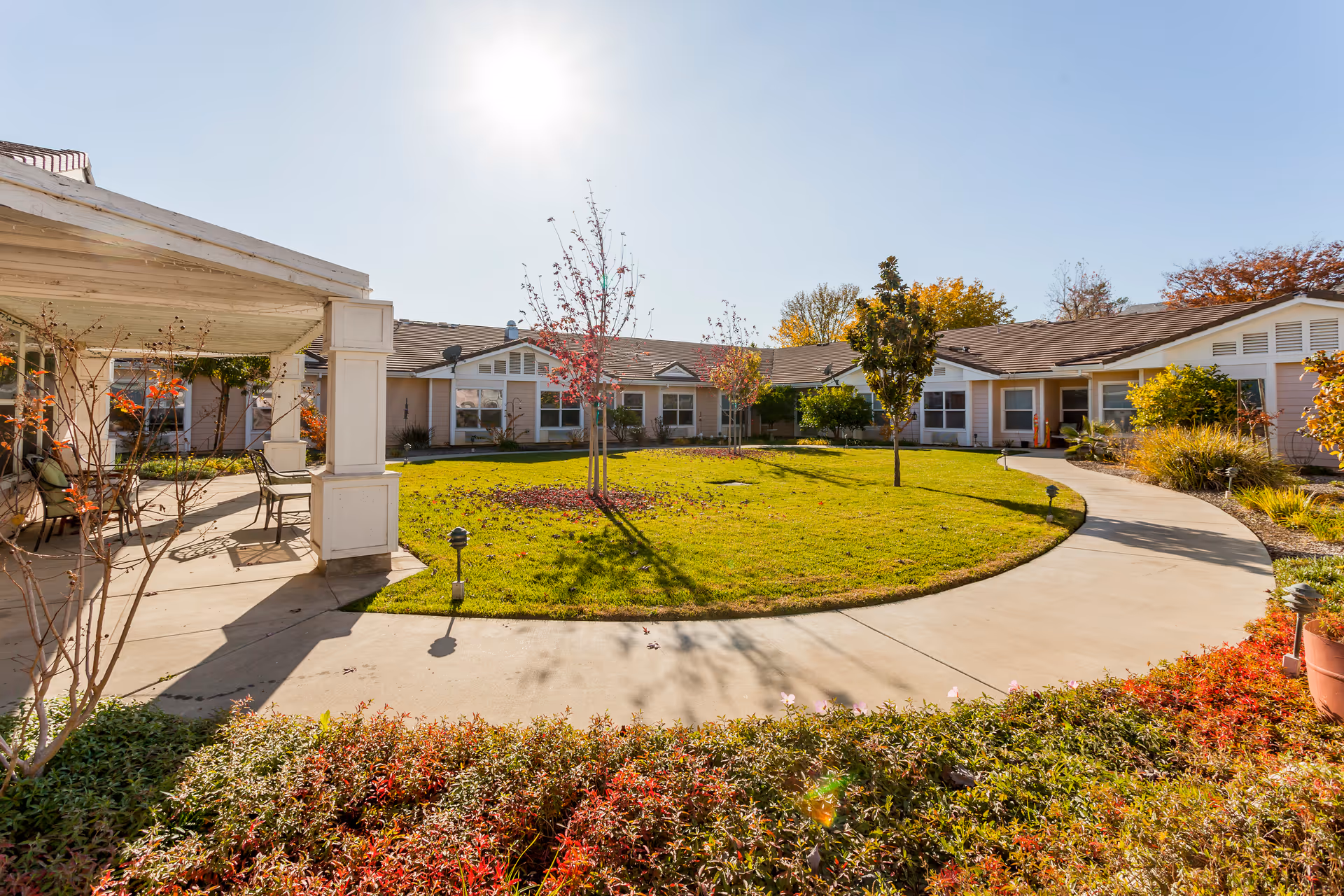 Sunny courtyard with a circular lawn surrounded by single-story senior living units and a covered patio.