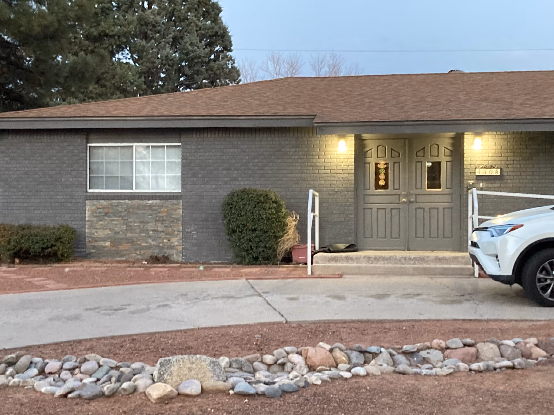 Single-story brick building front with illuminated double doors, a window to the left, landscaping rocks in front and a white SUV parked to the right.
