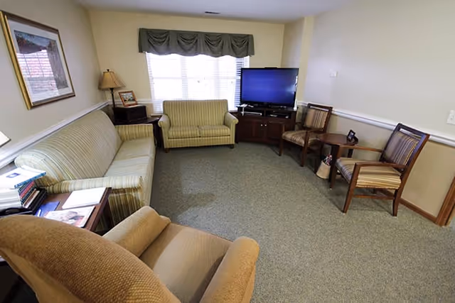 Cozy common living room with a sofa, loveseat, armchairs, a flat-screen TV on a cabinet, and a window with a valance.