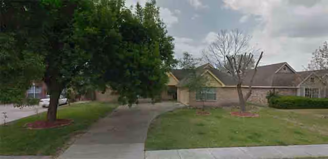 Single-story brick residential building with a driveway, front lawn, and trees.