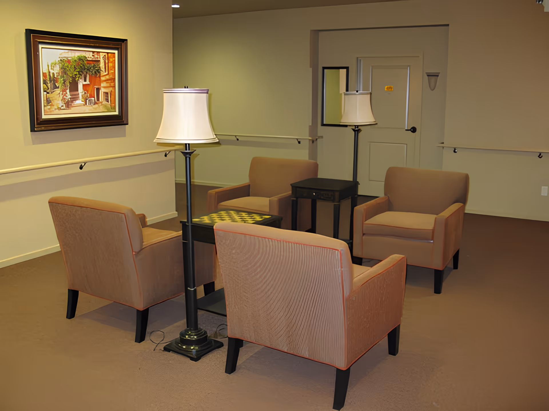 Small sitting area with four armchairs arranged around side tables and two floor lamps in a neutral-toned interior hallway.