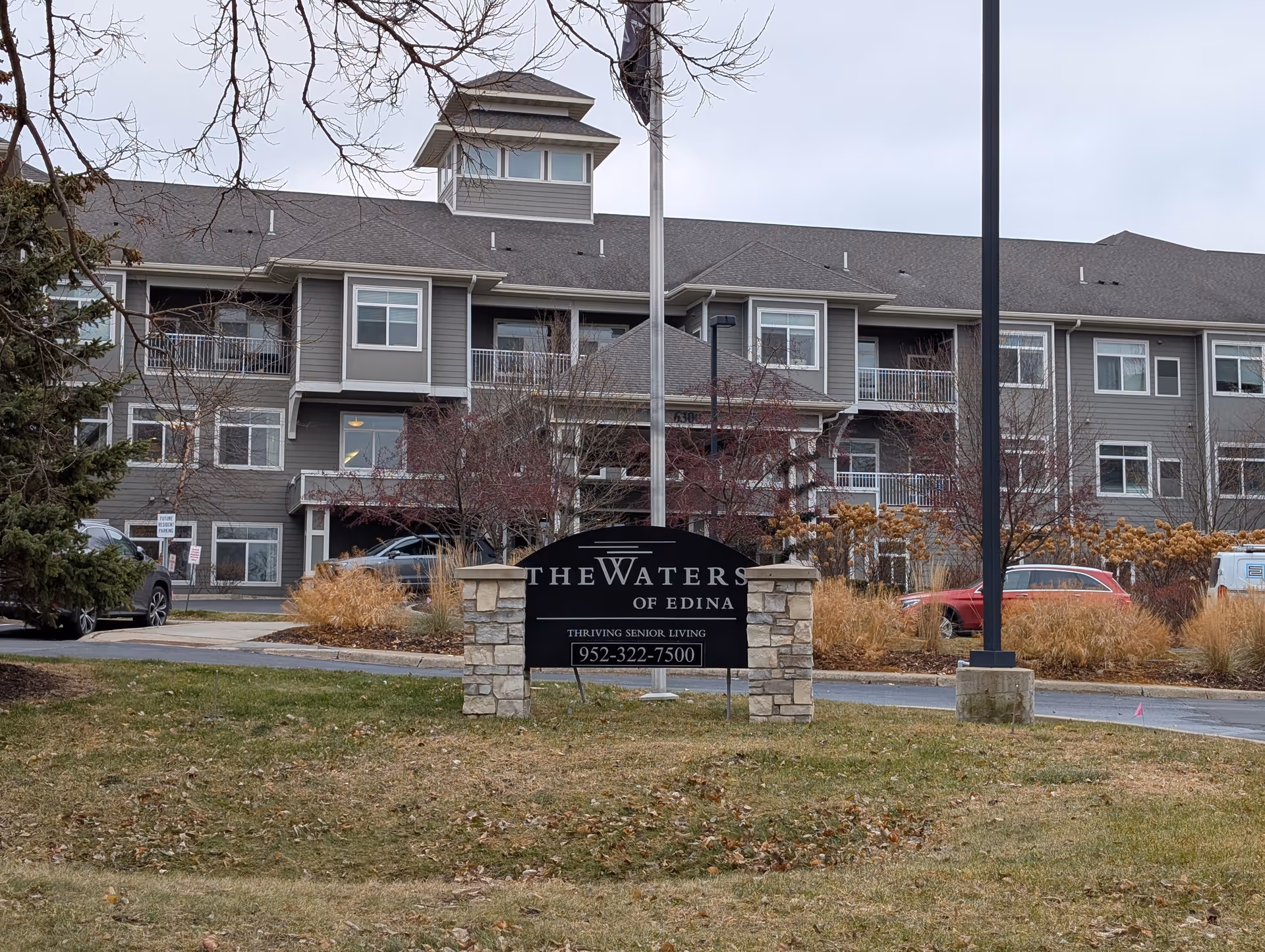 Exterior view of a multi-story senior living building with a stone sign reading 'The Waters of Edina' in the foreground.