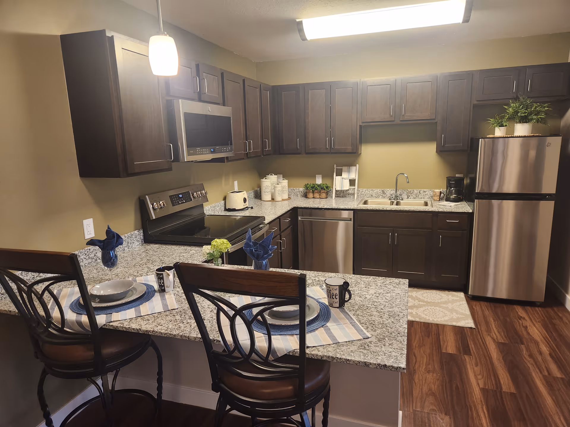 Modern kitchen with granite countertops, dark cabinets, stainless steel appliances, and a breakfast bar set for two.