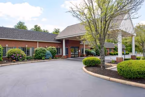 Exterior view of Life Care Center of Attleboro with driveway, trees, and entry porte-cochere.