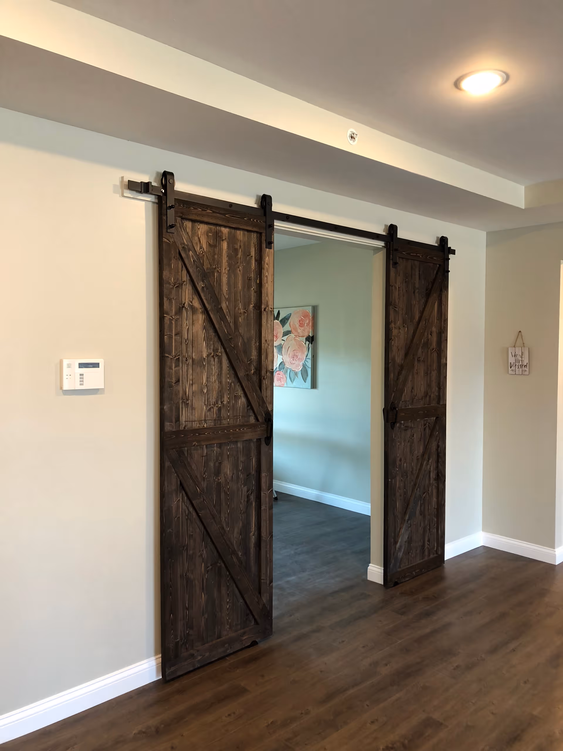 Interior view of sliding rustic wooden barn doors opening into a room with hardwood floors and floral wall art.