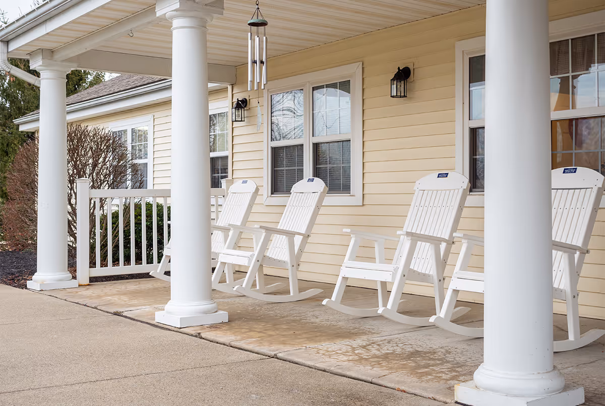 Covered front porch with white rocking chairs, columns, and windows on a pale yellow building.