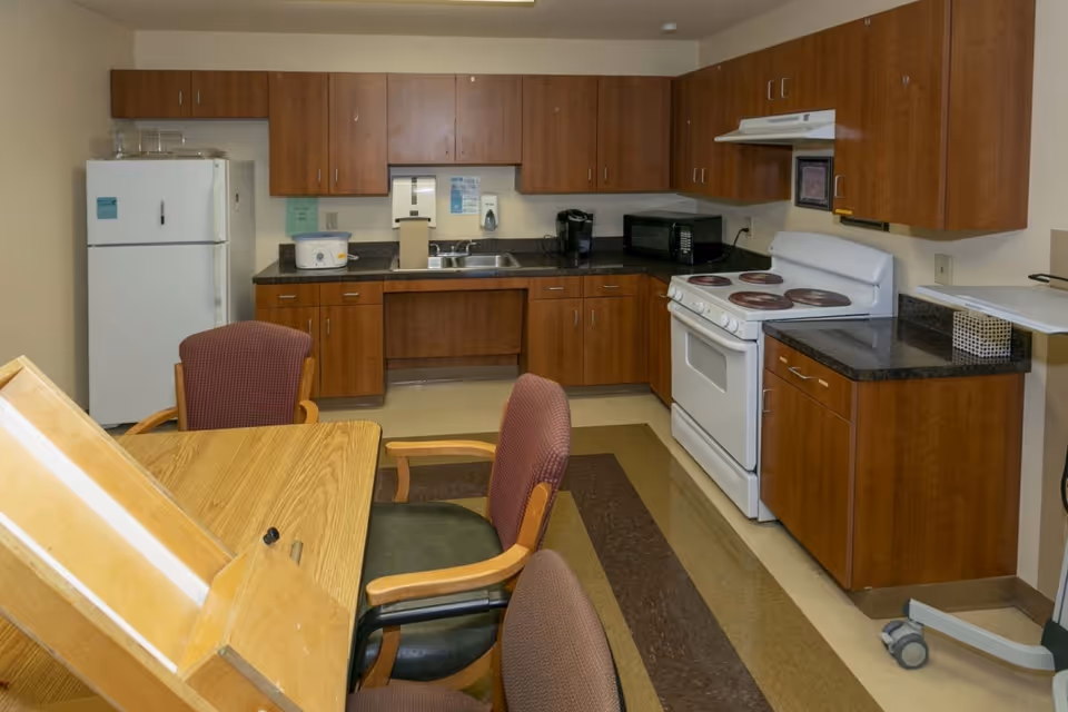 Communal kitchen and dining area with wooden cabinets, white appliances, a sink, microwave, and a table with chairs.
