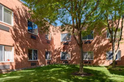Red brick building surrounds a grassy courtyard with trees and windows.
