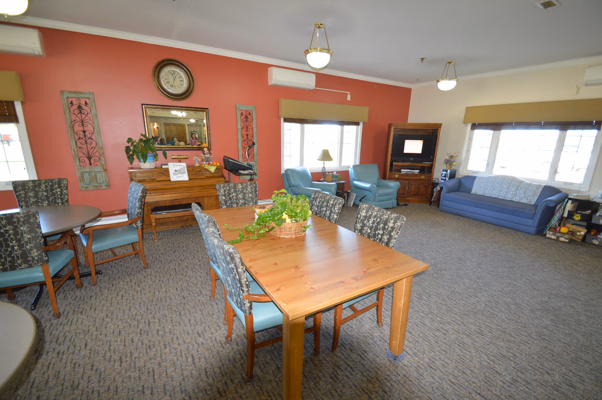Communal living room and dining area with tables, chairs, sofas, and a television.