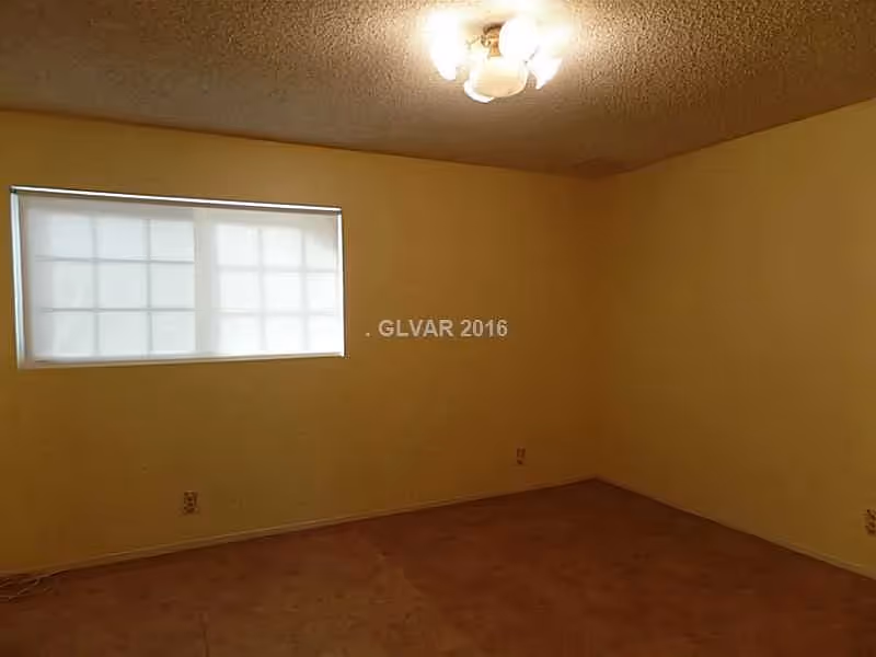 Empty room with beige walls and carpet, a window with closed blinds, and a ceiling light fixture.
