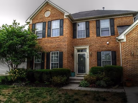 Two-story brick building with front door, windows, and trimmed shrubs.