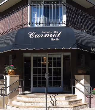 Brick building entrance with steps and a black awning reading "Beverly Hills Carmel North" over glass double doors.