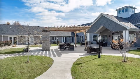 Outdoor courtyard of a senior living facility with a pergola, patio seating, and walkways in front of the building.