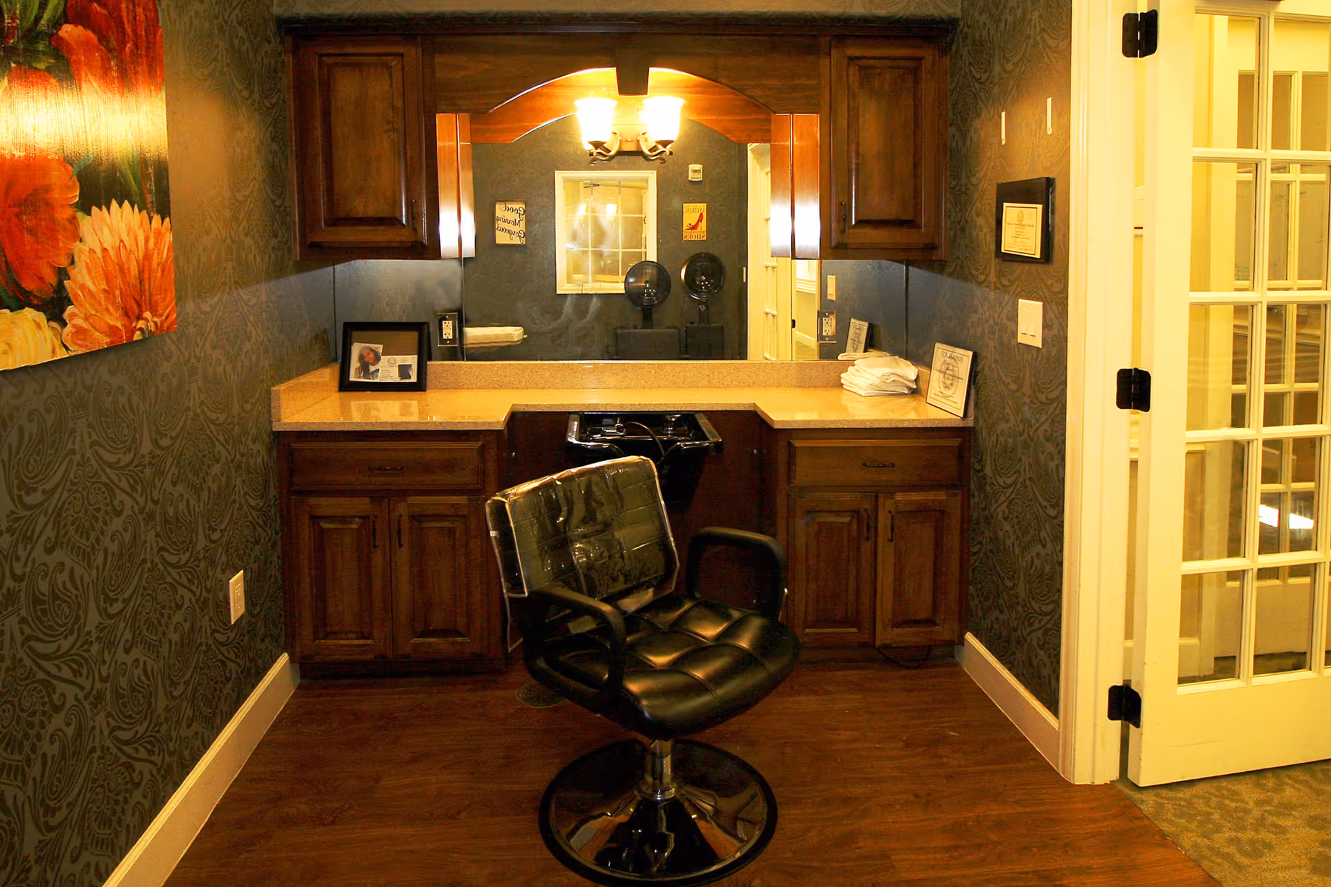 Interior salon area with a black styling chair facing a countertop, mirror, and wooden cabinets.