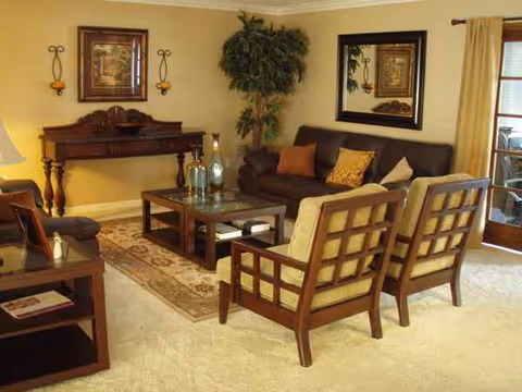 A cozy senior living room with beige walls, seating, and a glass coffee table.