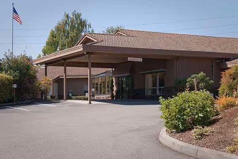 Exterior view of a senior living facility with a covered entrance and parking lot