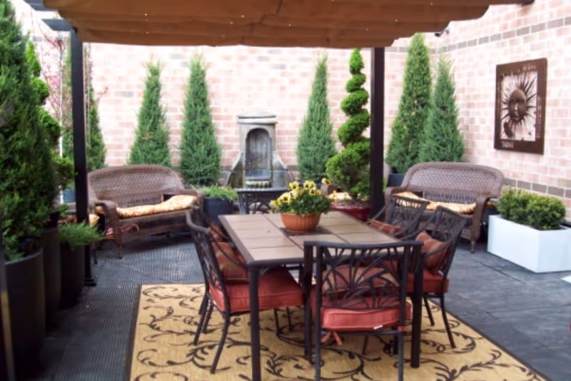 Covered outdoor patio with a dining table and chairs, wicker seating, potted plants, and a wall fountain.