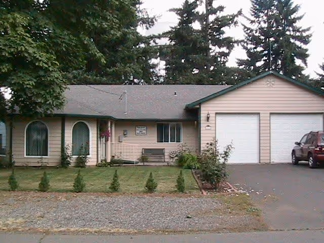 Single-story ranch-style house with a double garage, driveway and a small front lawn with trees.
