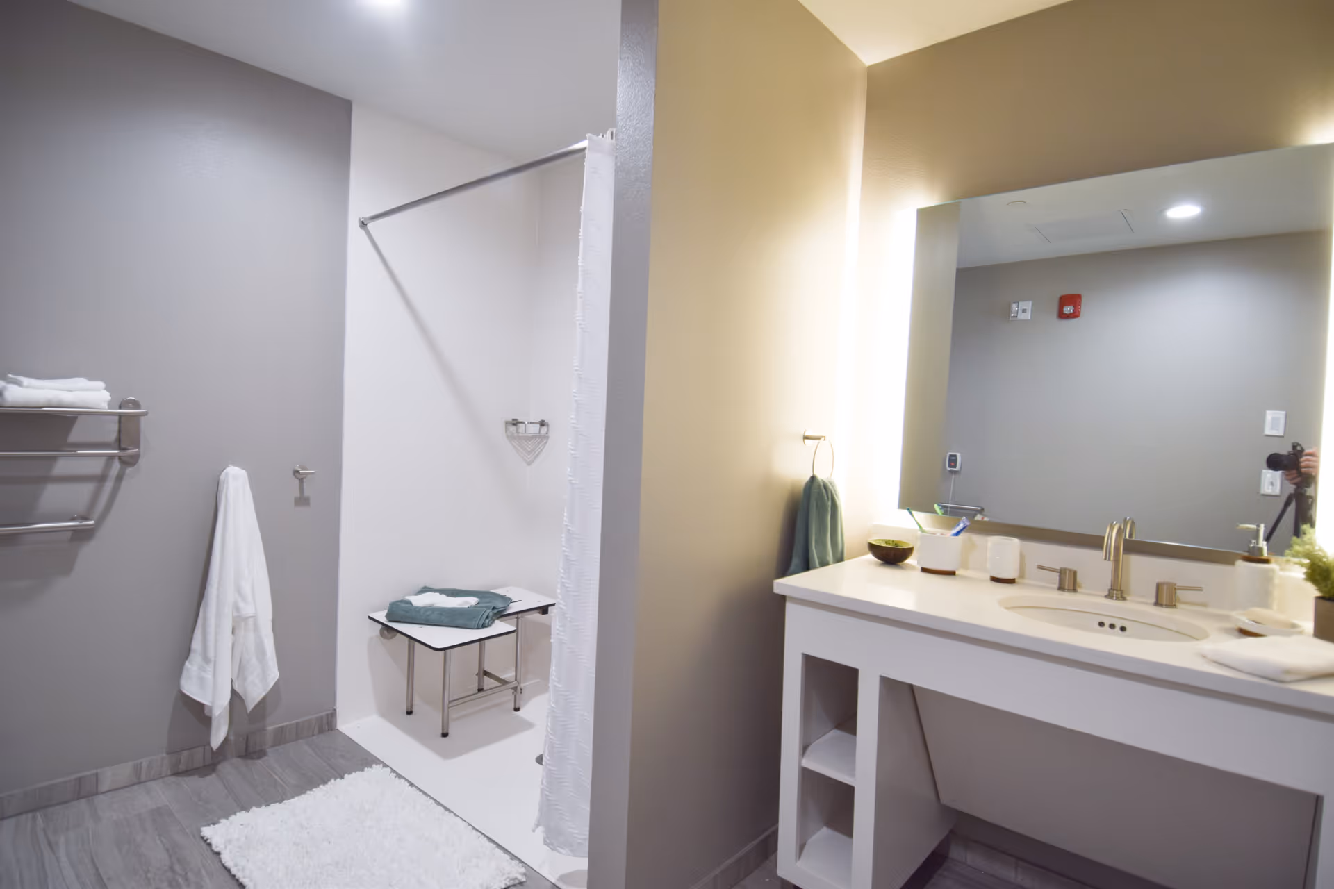 Bright modern bathroom with a walk-in shower, bench, vanity and illuminated mirror with towels.