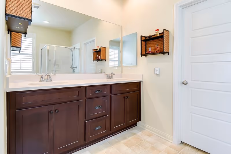 Bright bathroom featuring a dark wood double-sink vanity, large mirror, and glass-enclosed shower.