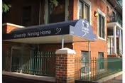 Brick building entrance with a blue awning that says University Nursing Home and a railing.