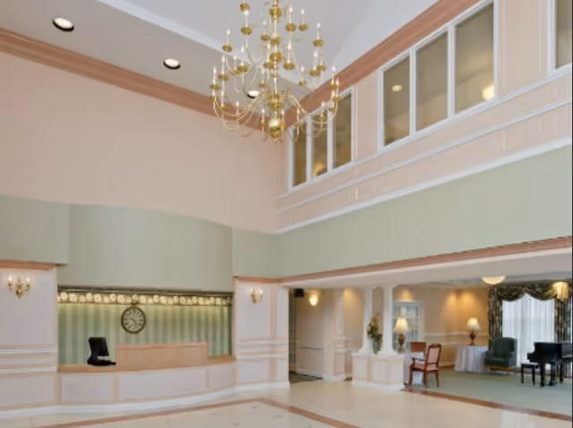 Spacious two-story lobby with a reception desk, chandelier, columns and a seating area.