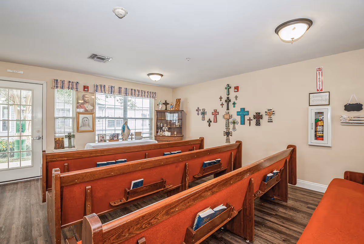 Small chapel-style room with wooden pews, a table at the front and crosses and religious images on the walls.