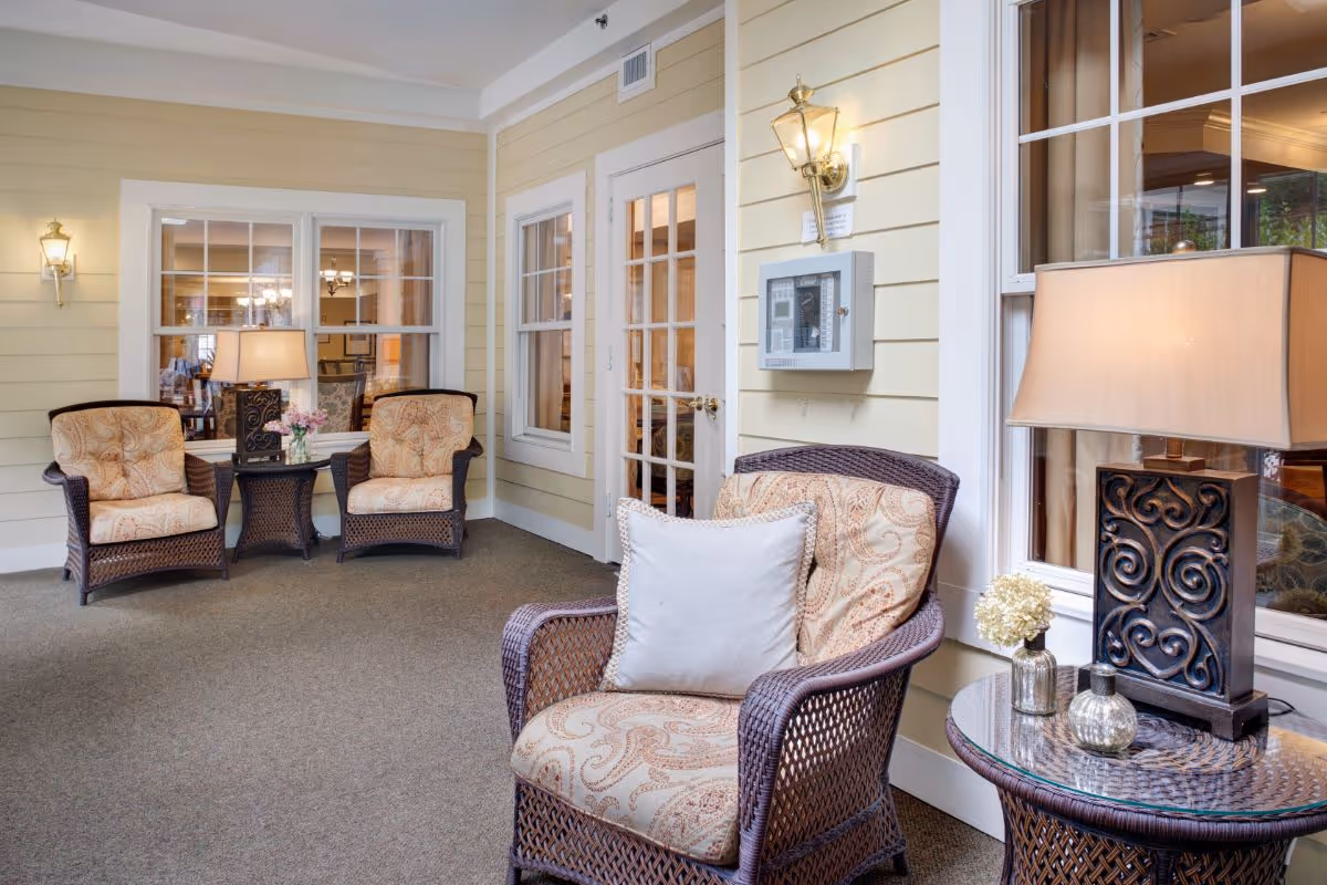 Cozy indoor seating area with wicker armchairs, side tables, lamps and windows.