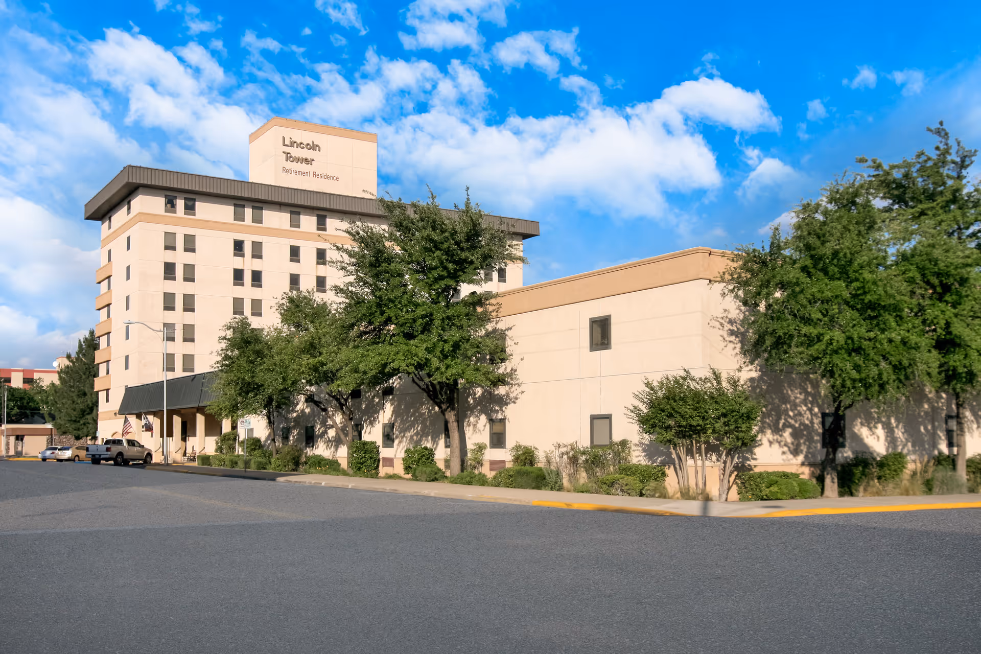 Exterior view of Holiday Lincoln Tower retirement residence with trees and blue sky.