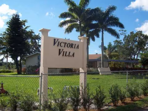 A Victoria Villa entrance sign beside a green lawn with tall palm trees.
