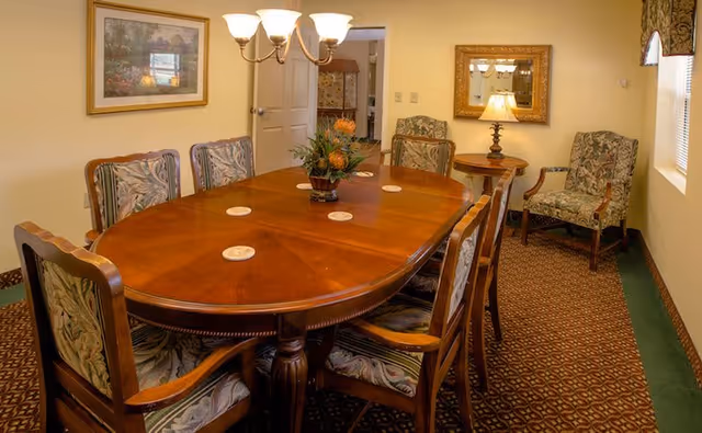Formal dining room featuring a polished oval wooden table surrounded by upholstered chairs, a chandelier overhead, and decorative artwork and mirror on the walls.