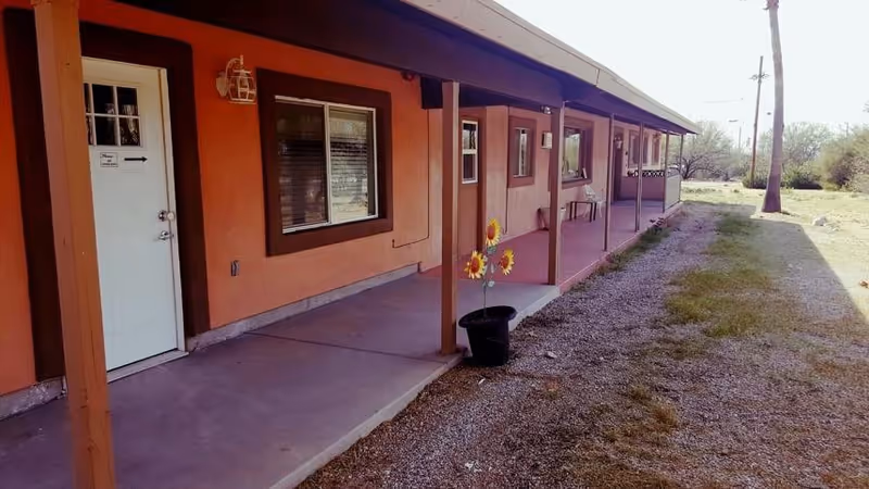 Exterior view of a single-story Venezia Place Assisted Living building with a covered porch and sunflowers.