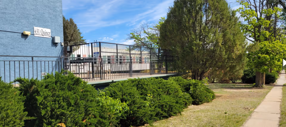 Exterior of a blue building with railing, walkway, and nearby trees and shrubs.