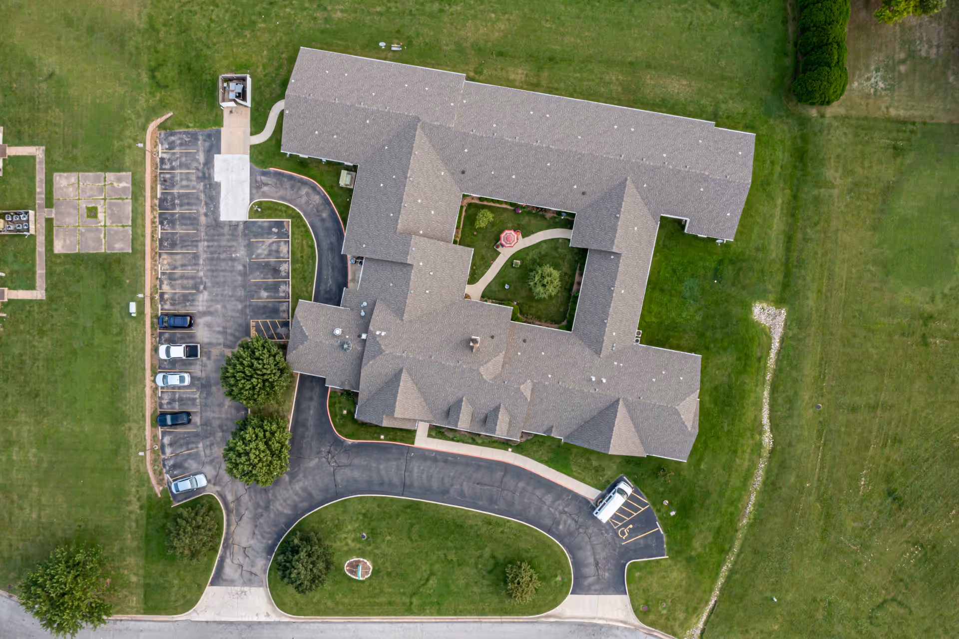Aerial top-down view of Alderbrook Village's U-shaped building with a central courtyard, parking lots, circular driveway, and surrounding lawns.