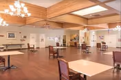 Spacious Rosewood Court senior living common area with wooden floors, tables, chairs, and chandeliers.