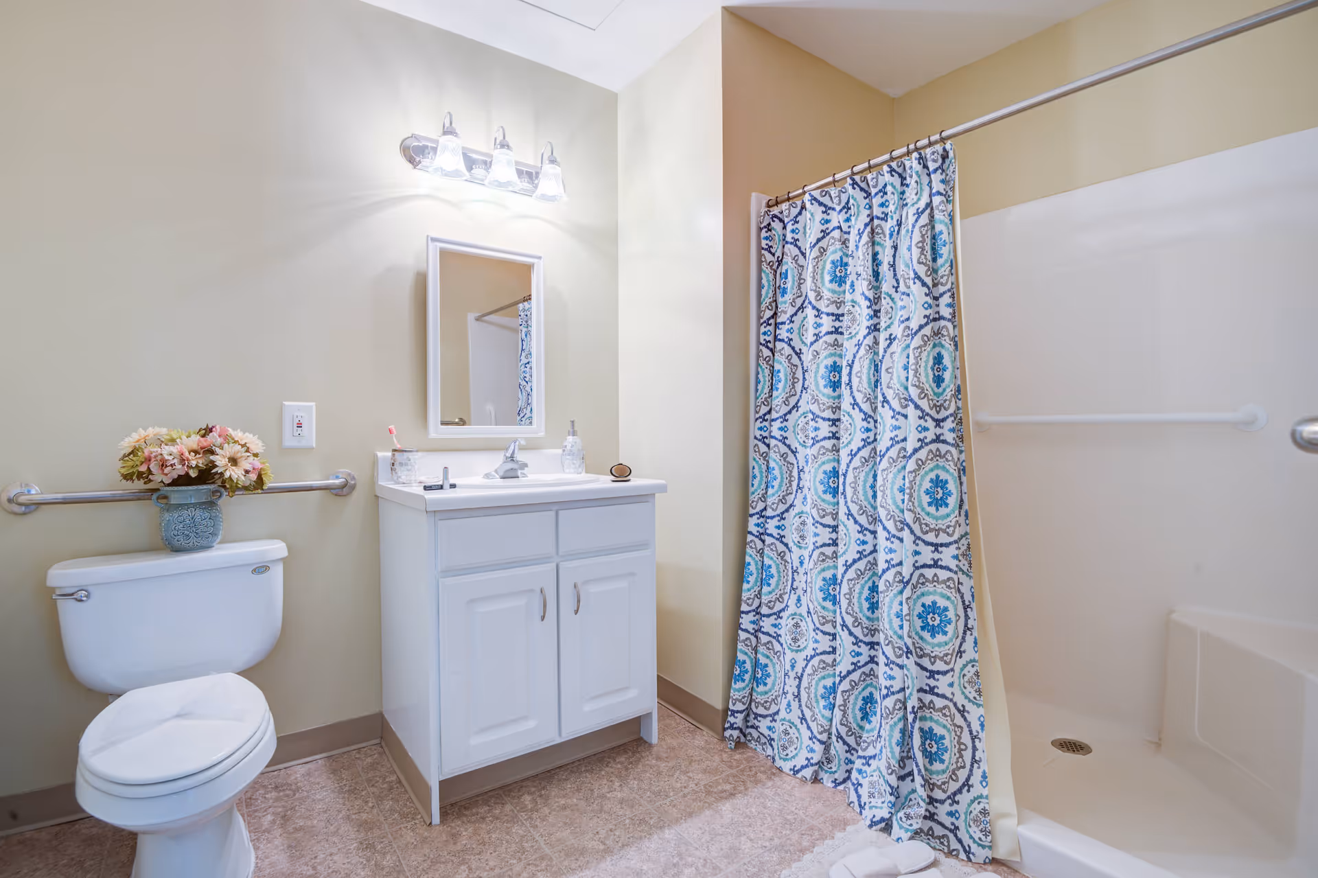 Bright bathroom with a toilet, white vanity and mirror, and a shower with a blue patterned curtain.