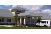 Light gray, modern senior living facility facade with glass entrance and a white vehicle parked nearby.