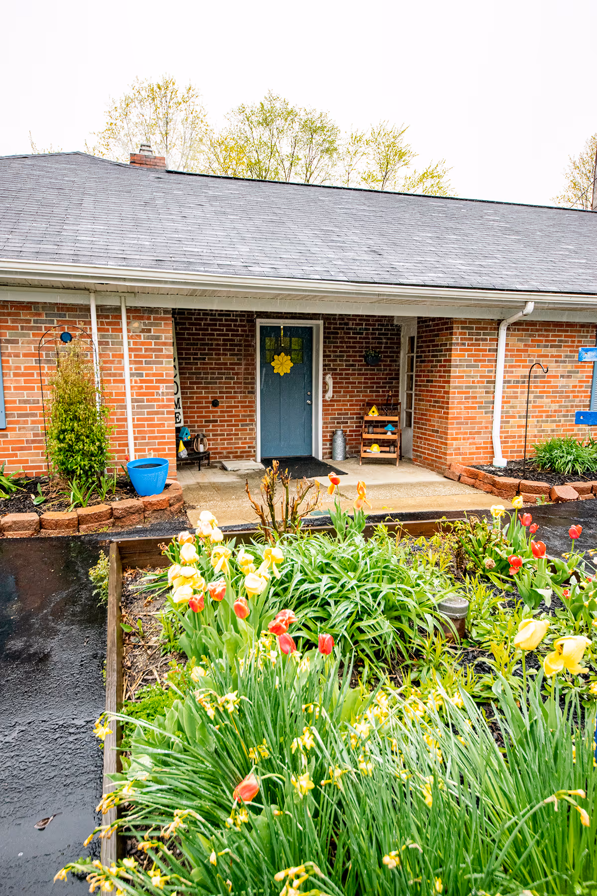Brick building front with a covered entry featuring a blue door decorated with a yellow flower and a foreground garden of red and yellow tulips.