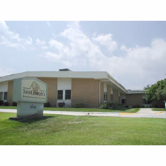 Exterior view of St. Joseph's Rehabilitation and Care Center building with a sign in the foreground on a grassy lawn under a partly cloudy sky.