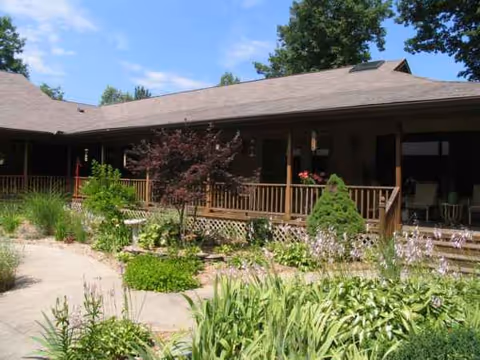 Exterior of Lakeshore Woods facility with a wooden porch and lush garden in front.
