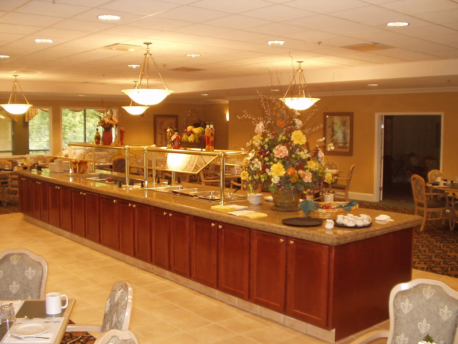 Spacious dining room with a long buffet counter, floral centerpiece, and pendant lighting.