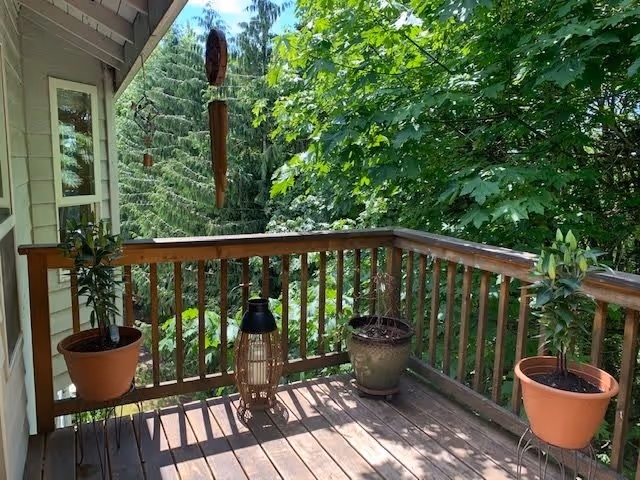 Wooden balcony deck with potted plants and a wind chime overlooking dense green trees.