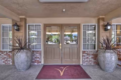 Front entrance with double brown doors, maroon mat, and two large planters.