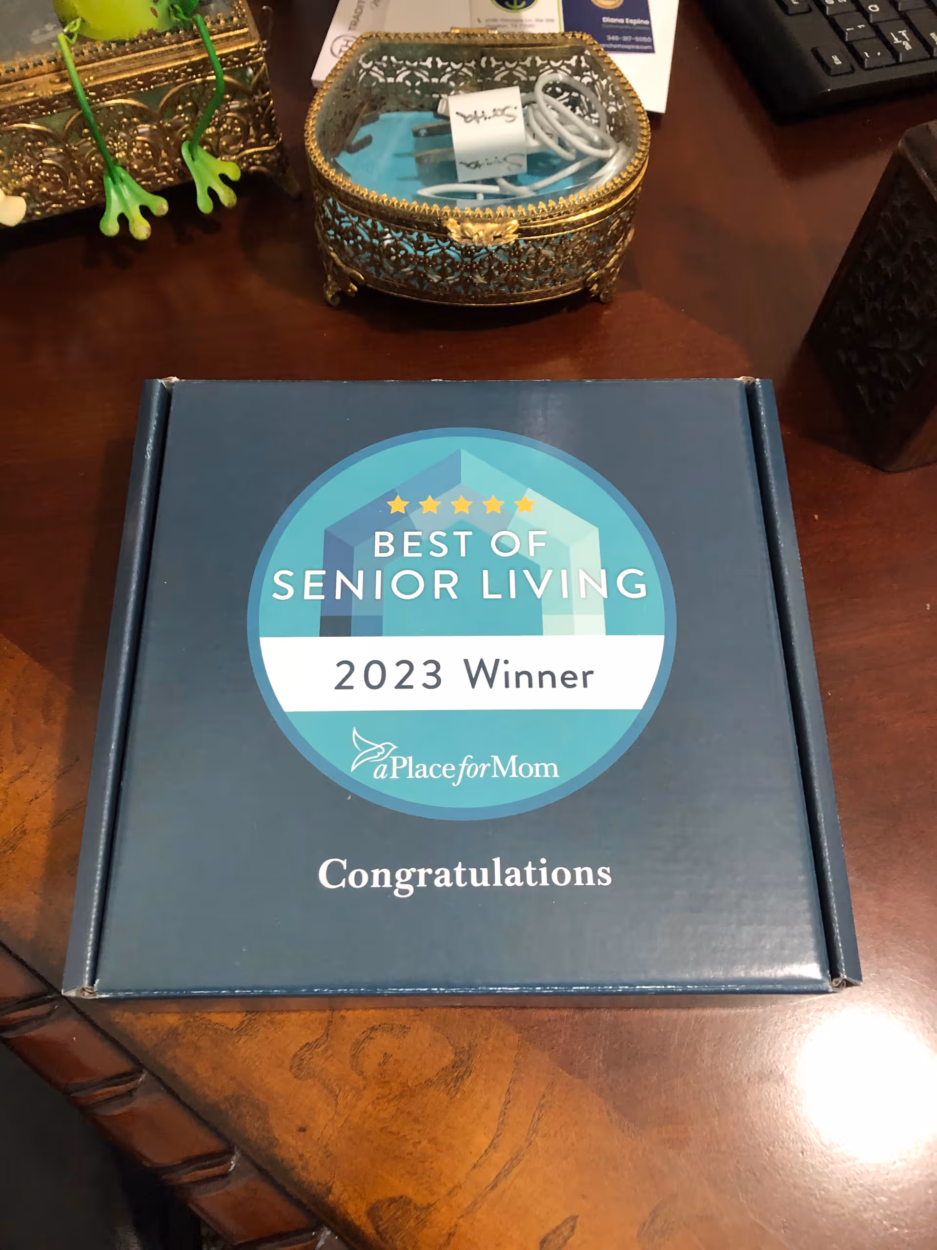 A boxed award on a wooden desk that reads "Best of Senior Living 2023 Winner" with decorative items and a keyboard nearby.