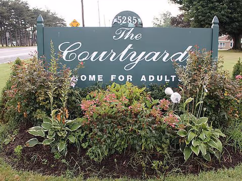 A green sign reading The Courtyard with Home for Adult lettering, surrounded by flowering shrubs.