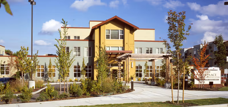 Front exterior of a modern three-story senior living building with landscaped grounds and a circular driveway.