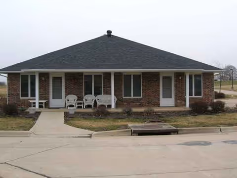 Brick, single-story facility facade with a small front porch and white chairs.