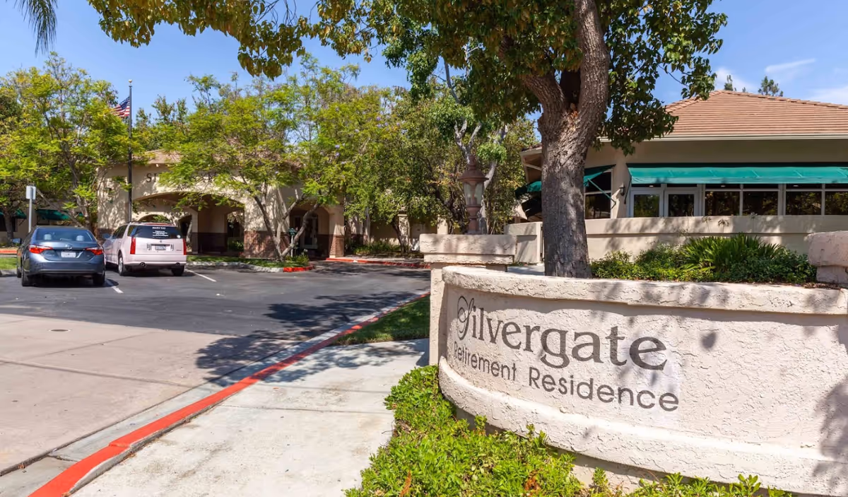 Exterior view of Silvergate Fallbrook Retirement entrance with sign, cars, and trees.