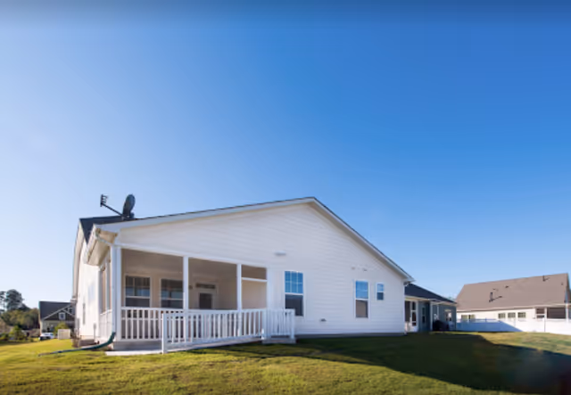 White single-story care home with a wraparound porch and green lawn under a blue sky.