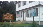 Exterior view of a two-story white building with an American flag near the entrance and a wooden sign that reads 'Autumn Villa'. There is a handicapped parking sign visible in front of the building.